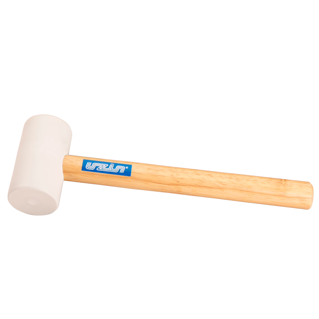 UZIN_Dummy_rubber hammer-UZIN_2014-11 Nærbillede af et gummihammer-produkt: lys beige gummihoved monteret på et glat lyst træskaft med en blå rektangulær mærkeetiket; hammeren ligger diagonalt på en ren hvid baggrund, blød jævn belysning fremhæver gummistruktur og træets årer; egnet til skånsomme slag ved træarbejde, montering eller fliselægning.